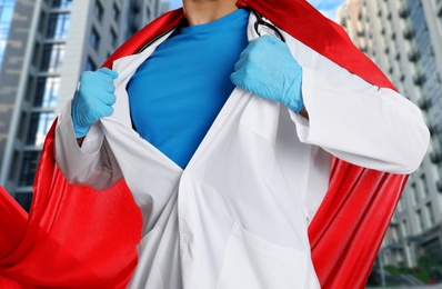 Doctor dressed as superhero on city background, closeup. Medical workers fighting with dangerous diseases