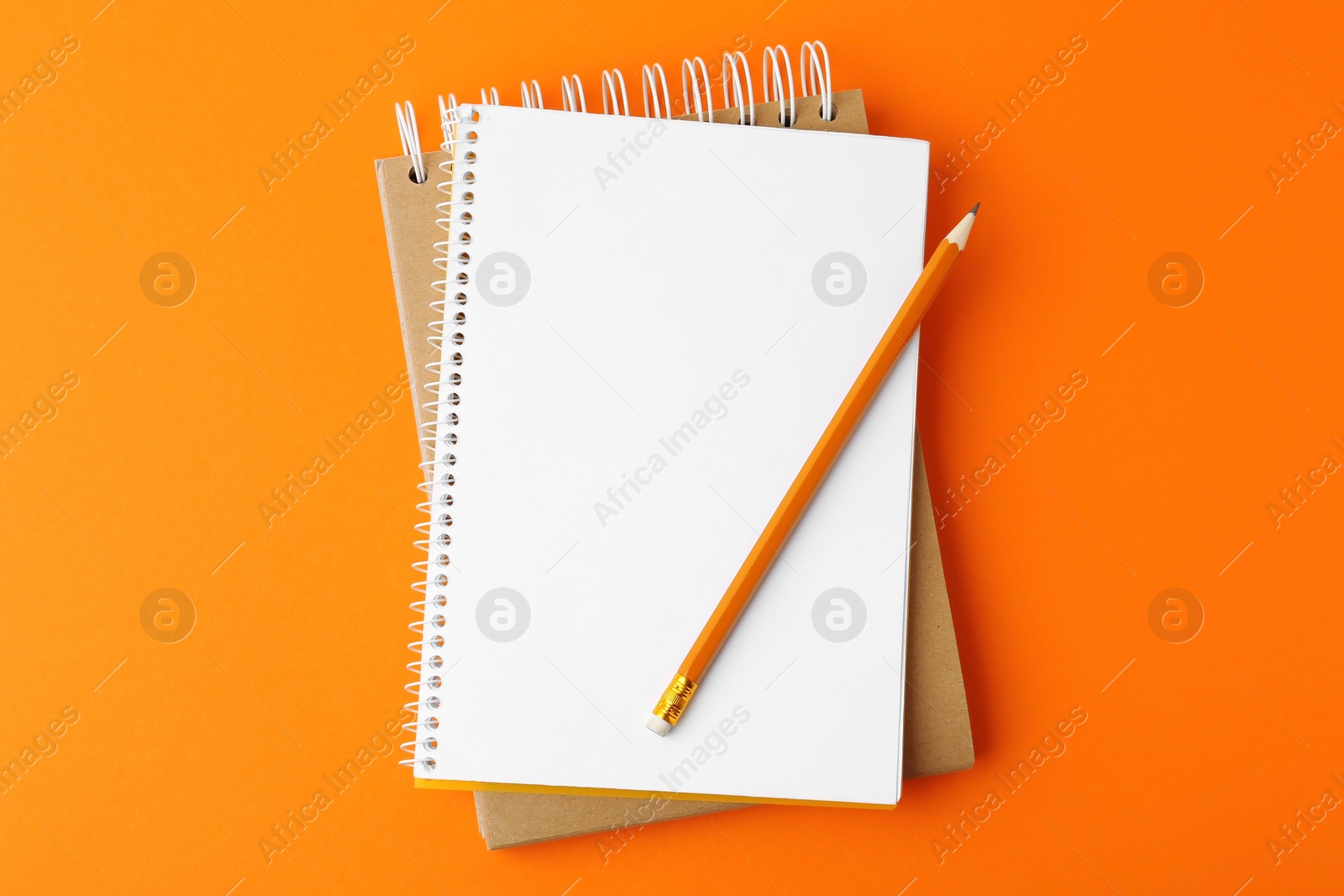 Photo of Notebooks with pencil on orange background, top view