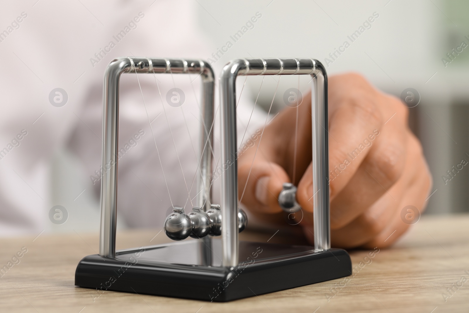 Photo of Man playing with Newton's cradle at wooden table, closeup. Physics law of energy conservation