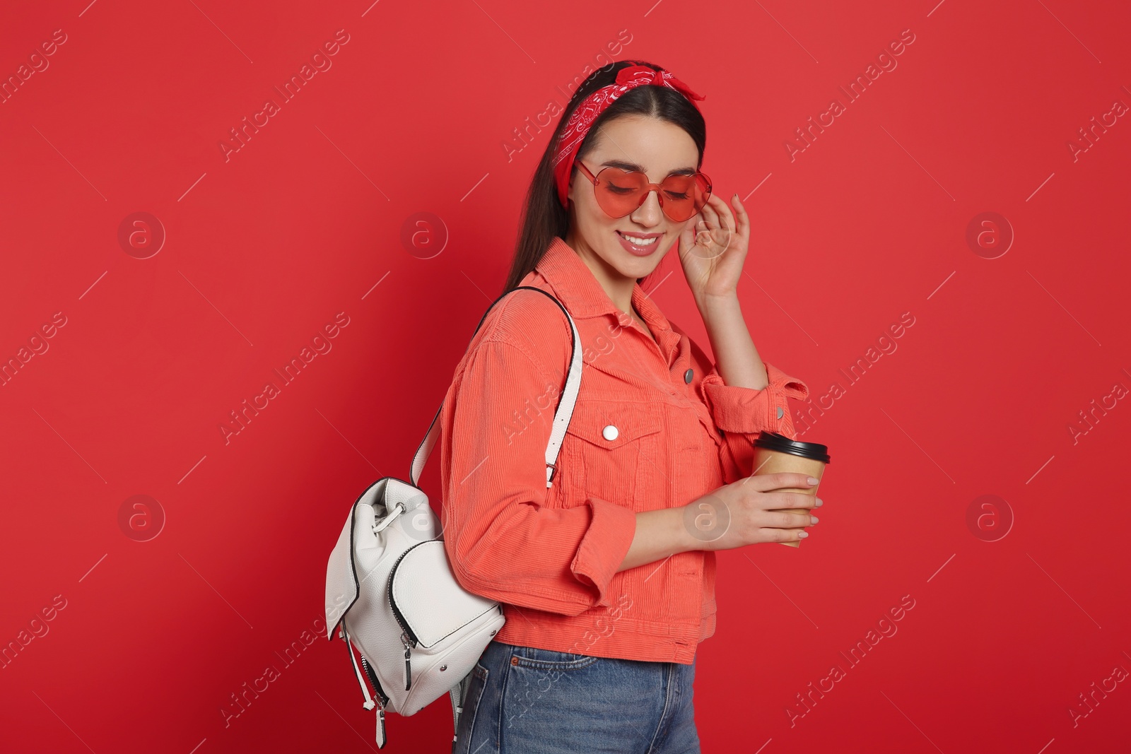Photo of Beautiful young woman with stylish leather backpack and cup of coffee on red background