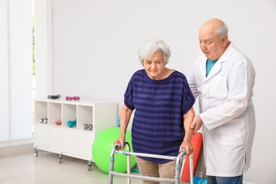 Doctor helping elderly woman with walking frame indoors