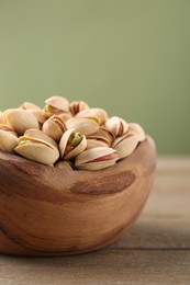 Photo of Tasty pistachios in bowl on wooden table against olive background, closeup