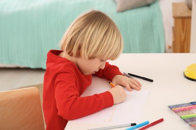 Photo of Little boy drawing at desk in room. Home workplace