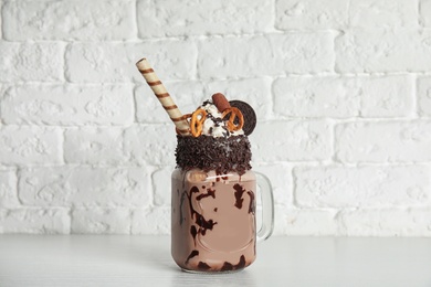 Photo of Mason jar of tasty milk shake with sweets on table near brick wall