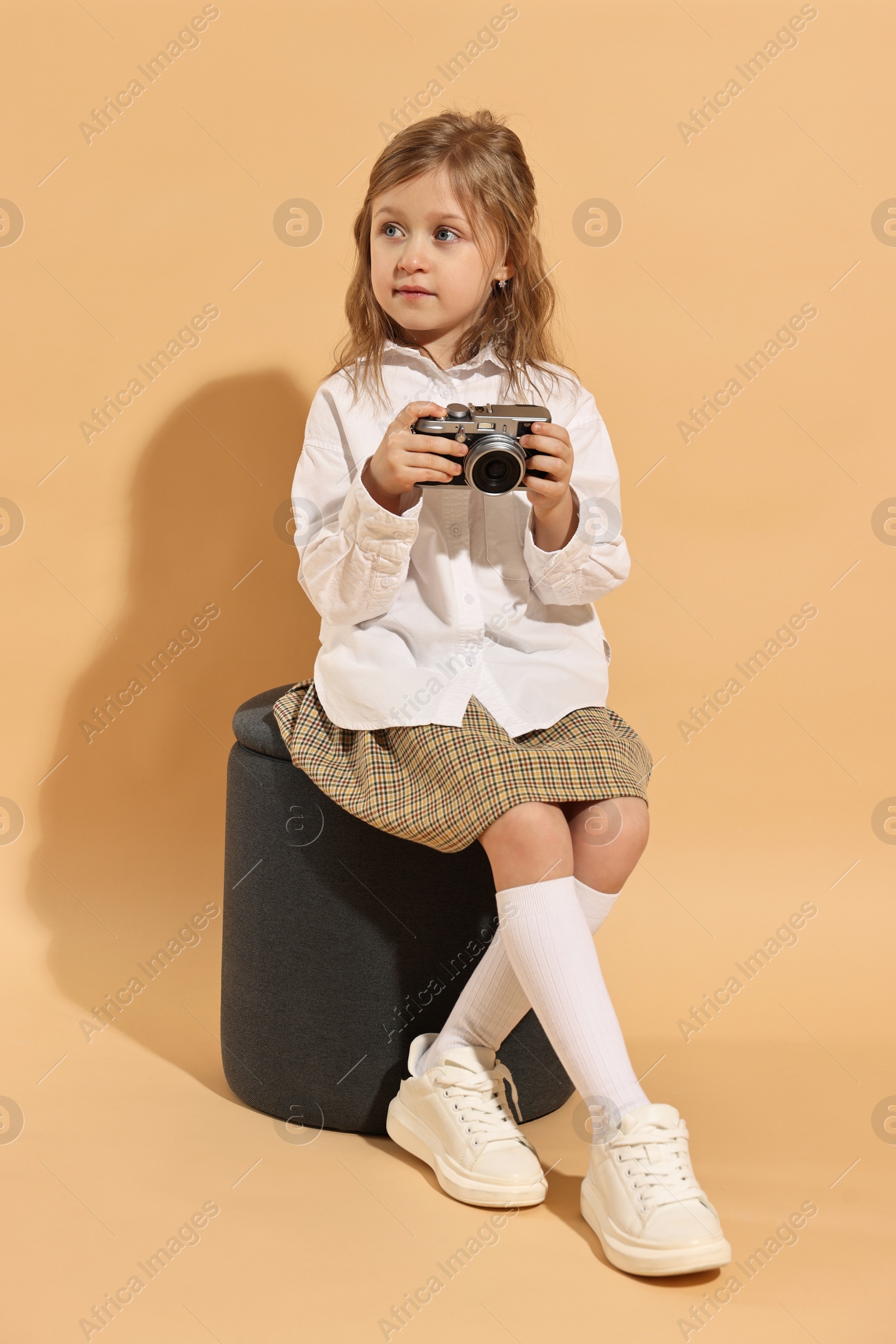 Photo of Fashion concept. Stylish girl with vintage camera on pale orange background