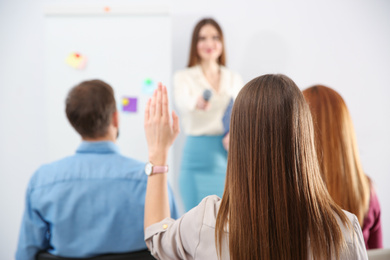 Young woman raising hand to ask question at business training indoors, back view