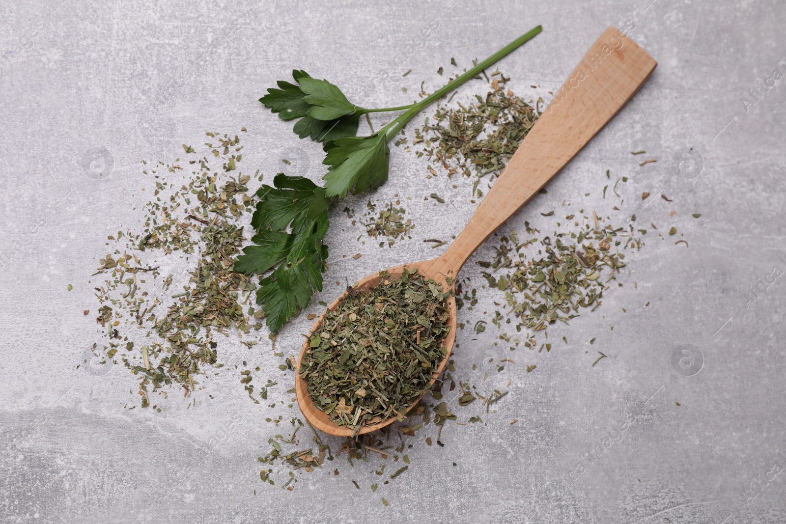 Photo of Wooden spoon with dried parsley and fresh leaves on light grey table, flat lay