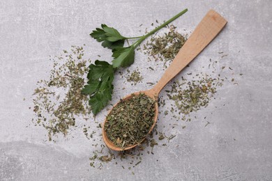 Wooden spoon with dried parsley and fresh leaves on light grey table, flat lay