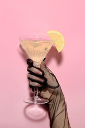 Photo of Woman holding martini glass of refreshing cocktail with lemon slice on pink background, closeup