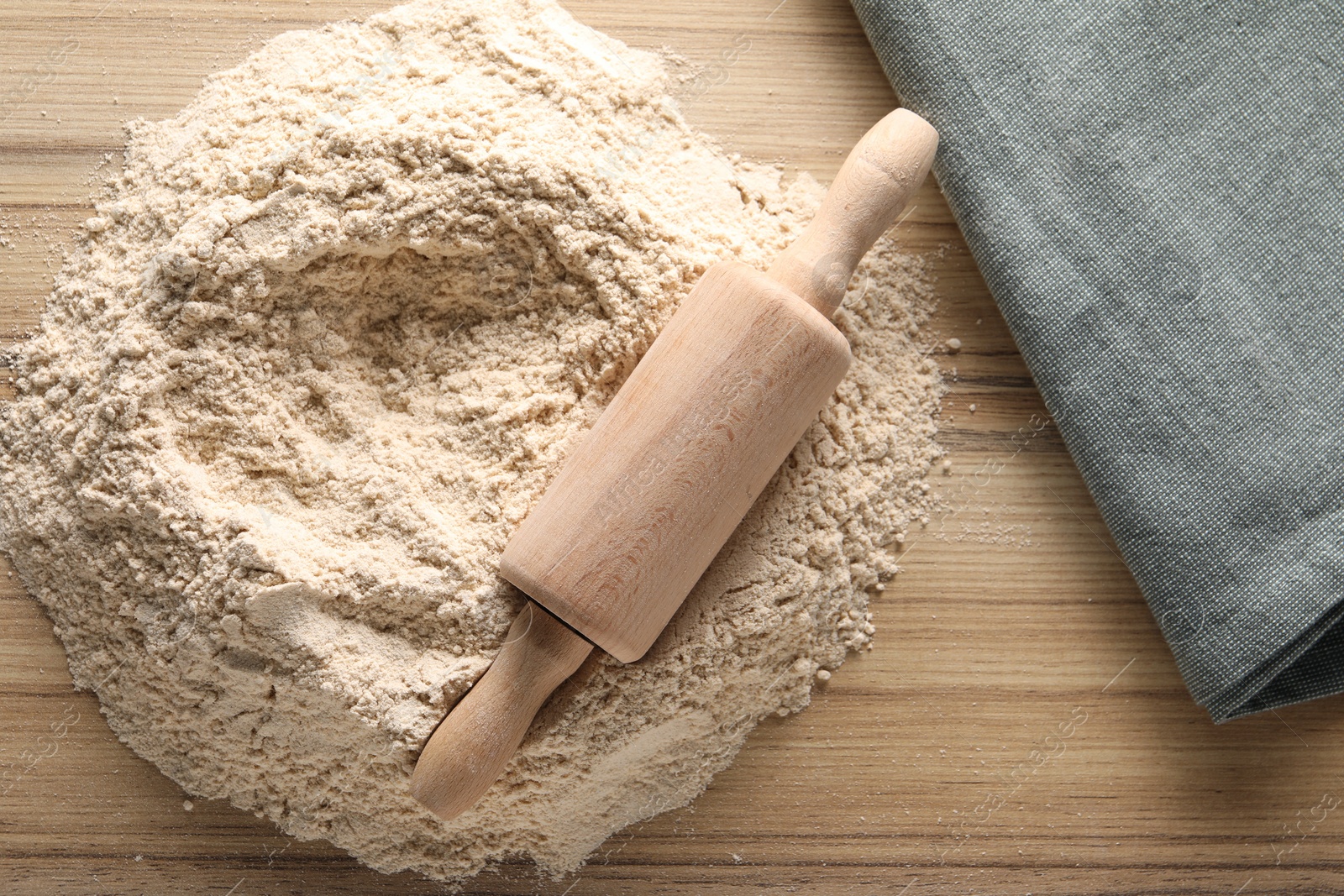 Photo of Pile of flour and rolling pin on wooden table, top view