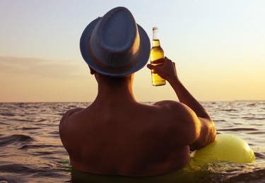 Photo of Young man with drink on inflatable ring in sea