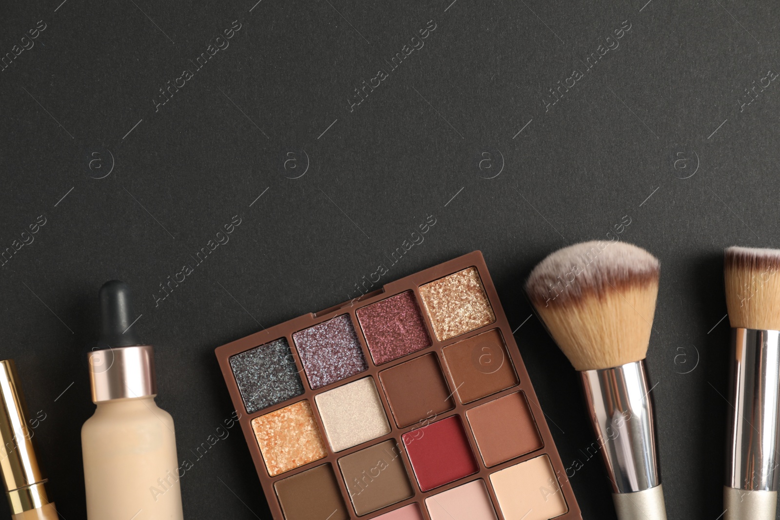 Photo of Eyeshadow palette with foundation and makeup brushes on dark background, flat lay. Space for text