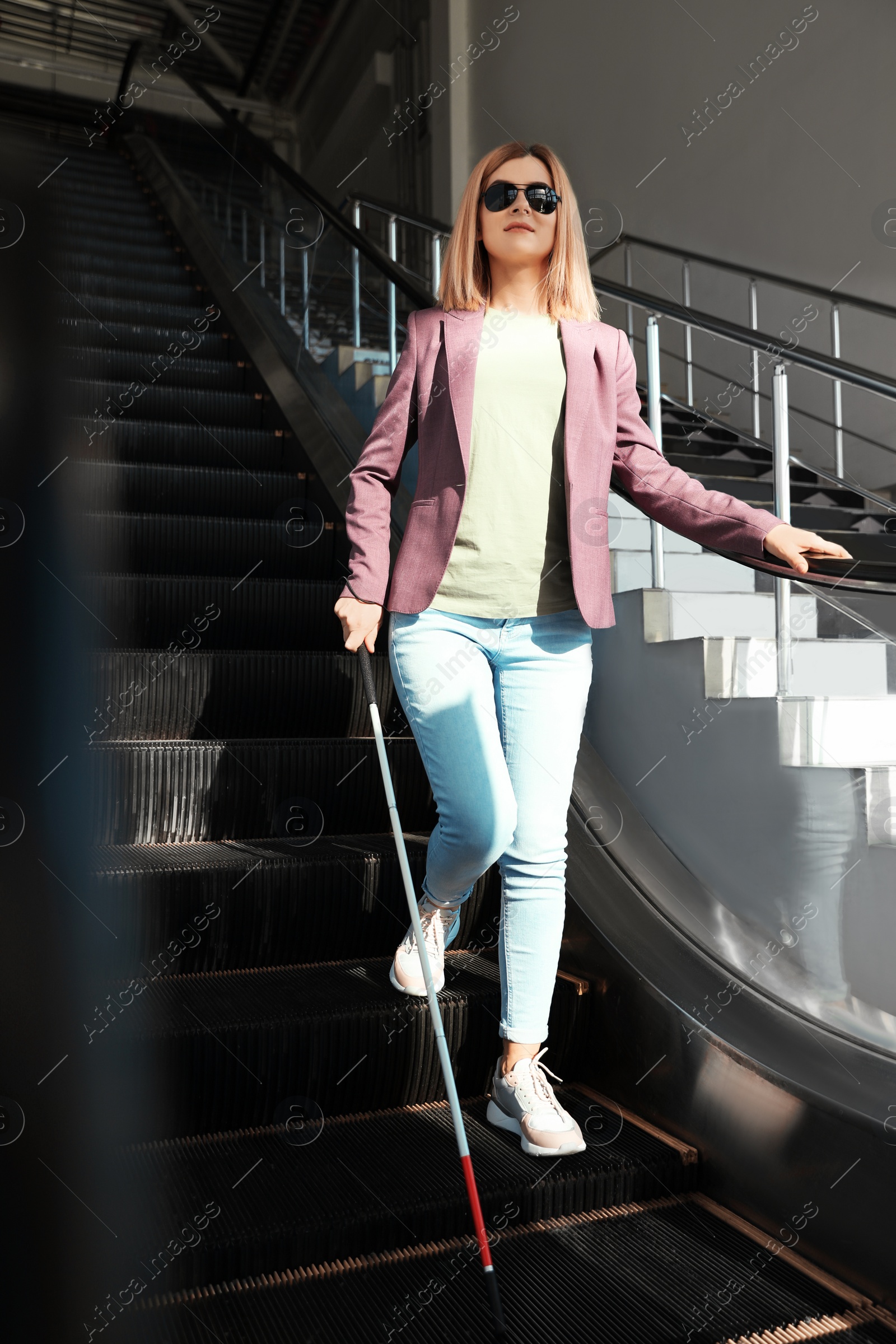 Photo of Blind person with long cane on escalator indoors