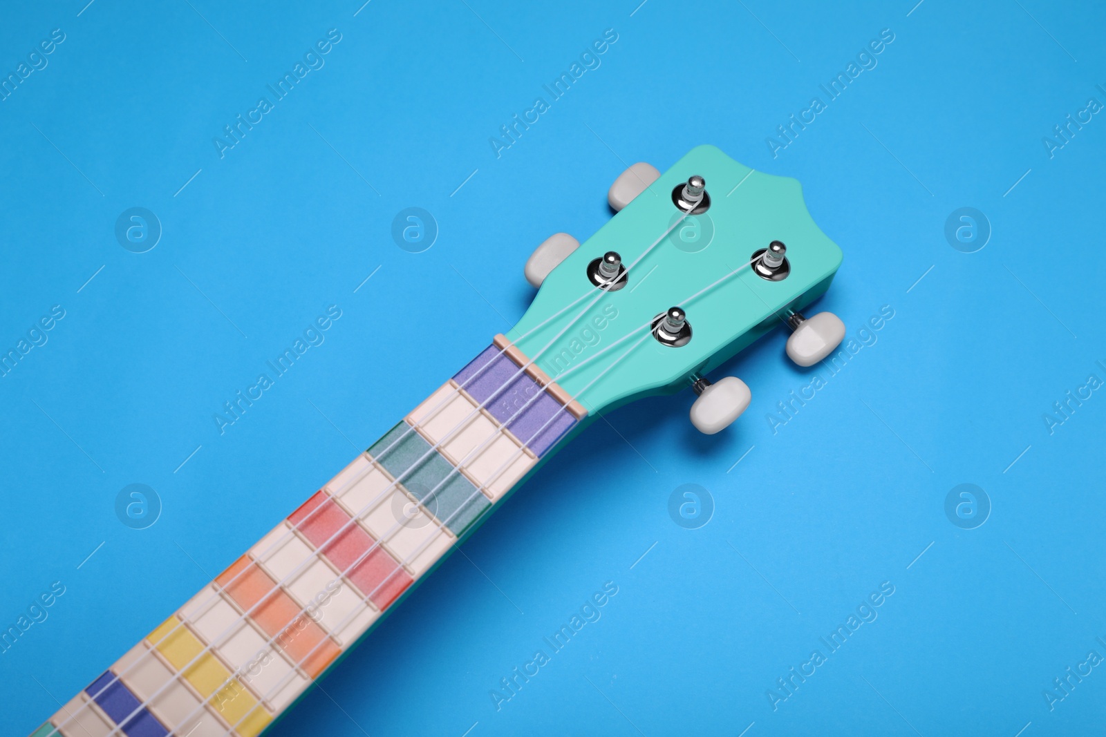 Photo of Colorful ukulele neck on light blue background, above view. String musical instrument