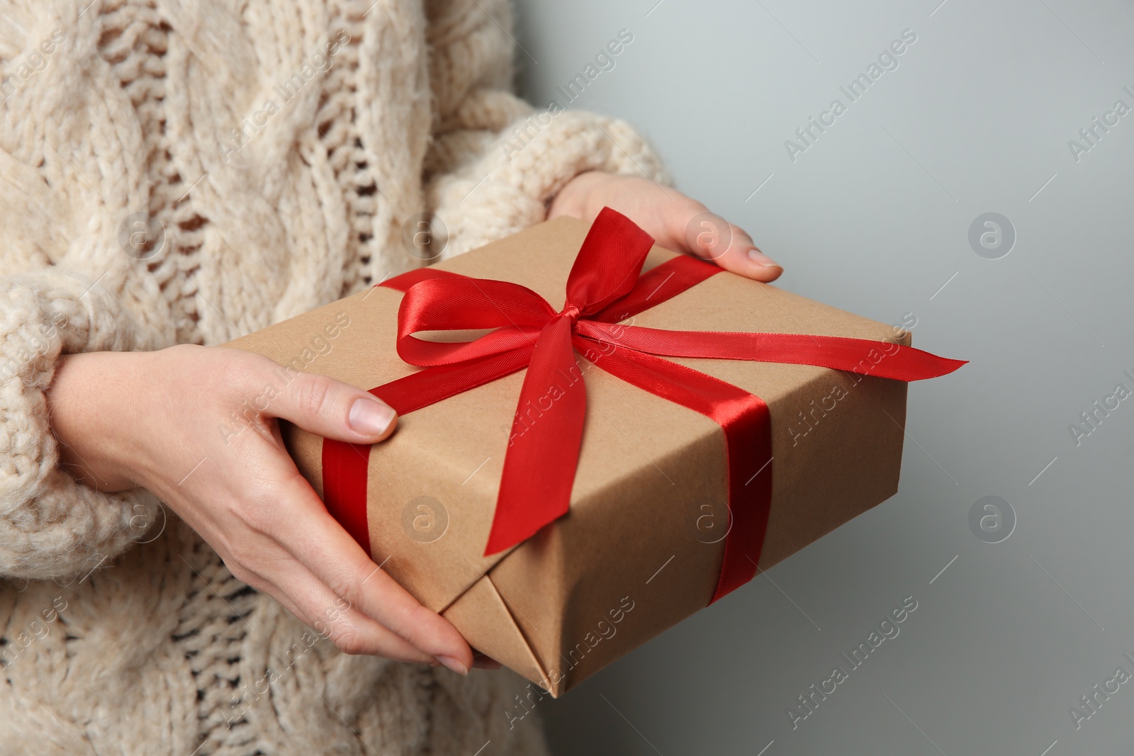 Photo of Woman holding Christmas gift box on grey background, closeup