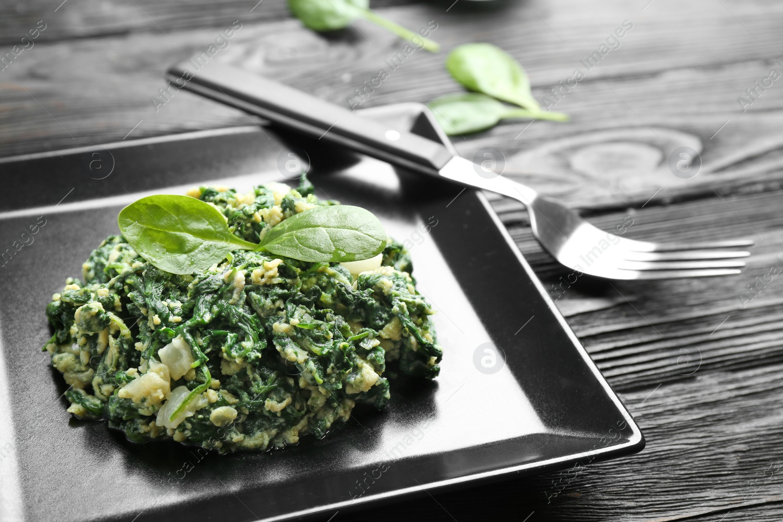 Photo of Plate with tasty spinach served on black wooden table, closeup. Healthy food