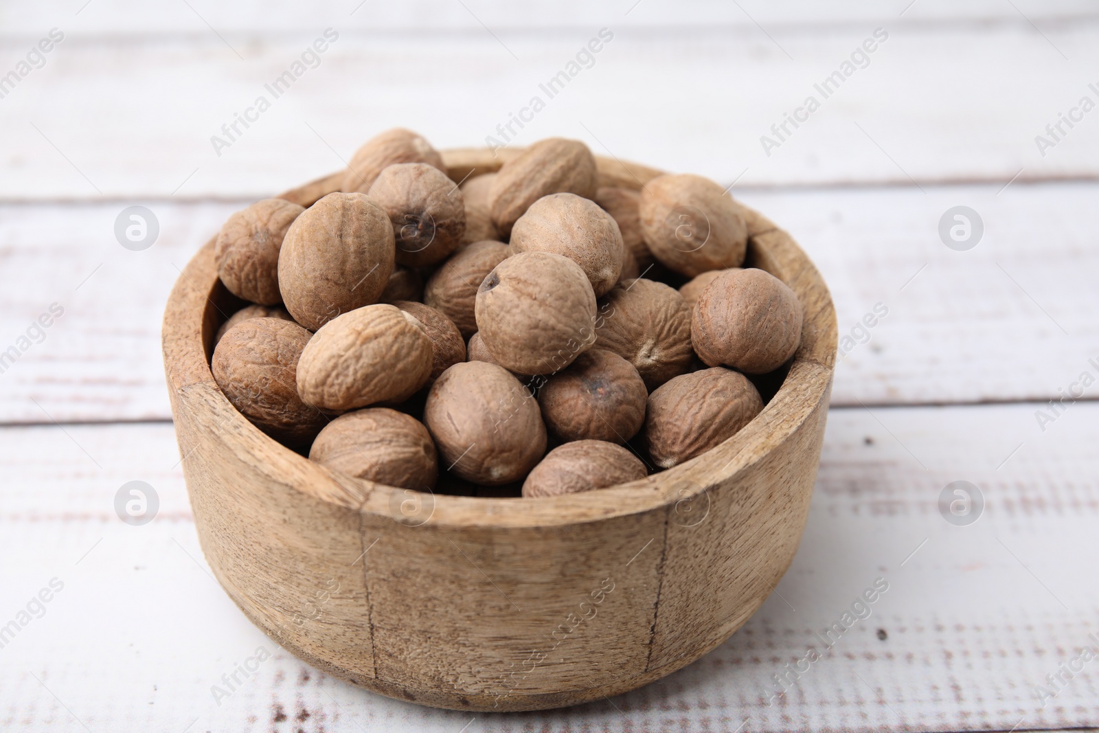 Photo of Whole nutmegs in bowl on light wooden table, closeup