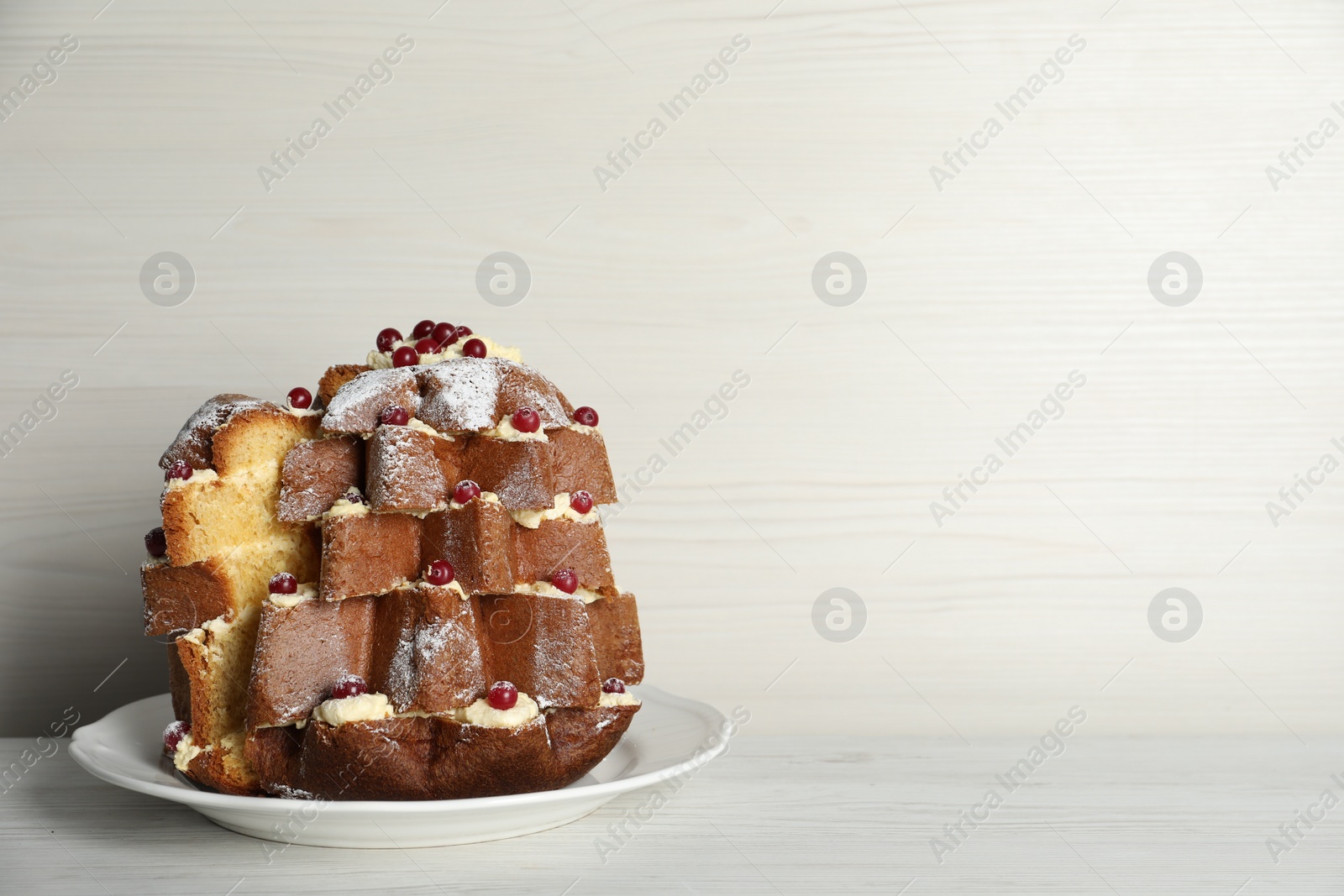 Photo of Delicious Pandoro Christmas tree cake with powdered sugar and berries on white wooden table. Space for text
