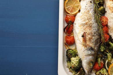 Photo of Delicious fish with vegetables and lemon in baking dish on blue wooden table, top view. Space for text