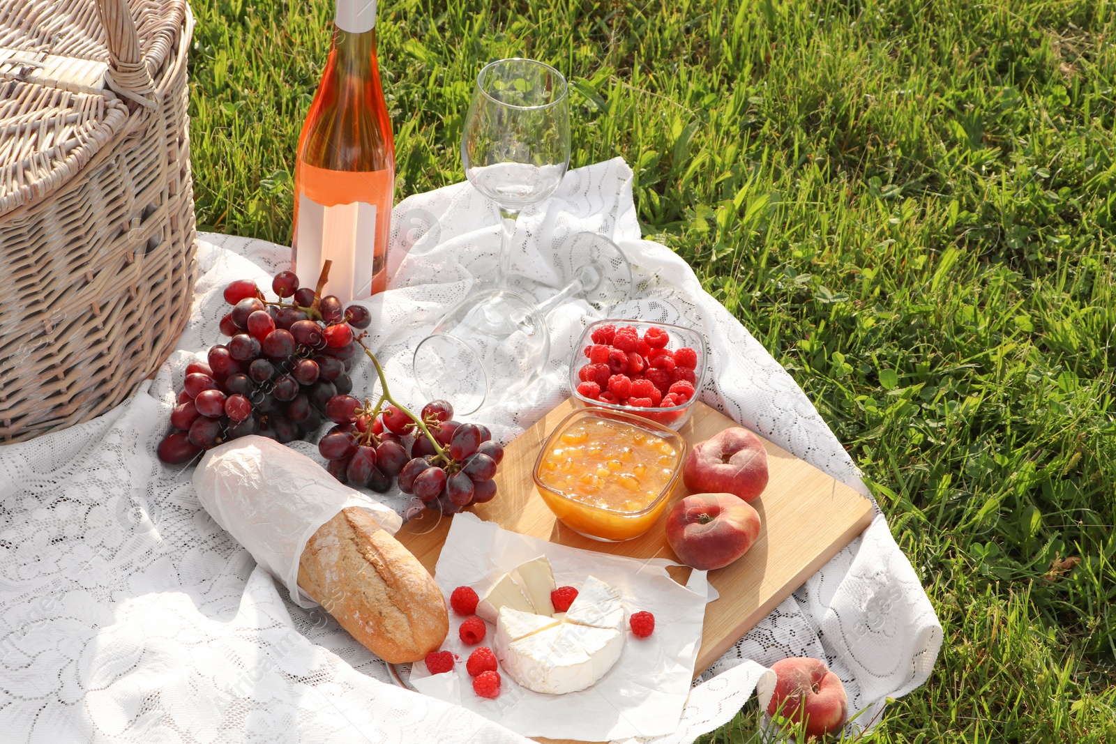 Photo of Picnic blanket with tasty food, basket and cider on green grass outdoors