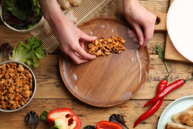 Photo of Woman making tasty spring roll at wooden table, top view