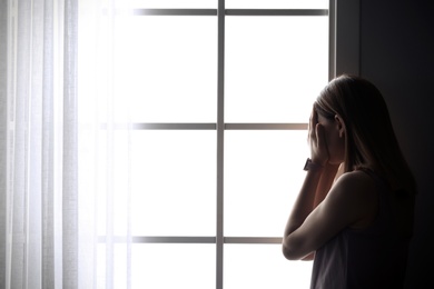 Lonely depressed woman near window at home