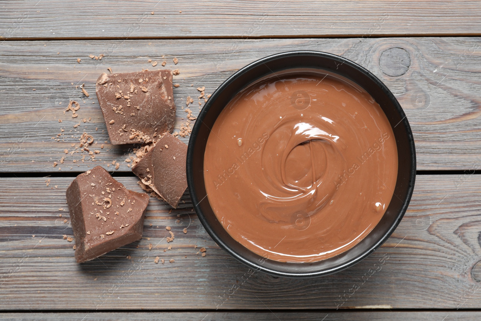 Photo of Tasty milk chocolate paste in bowl and pieces on wooden table, top view