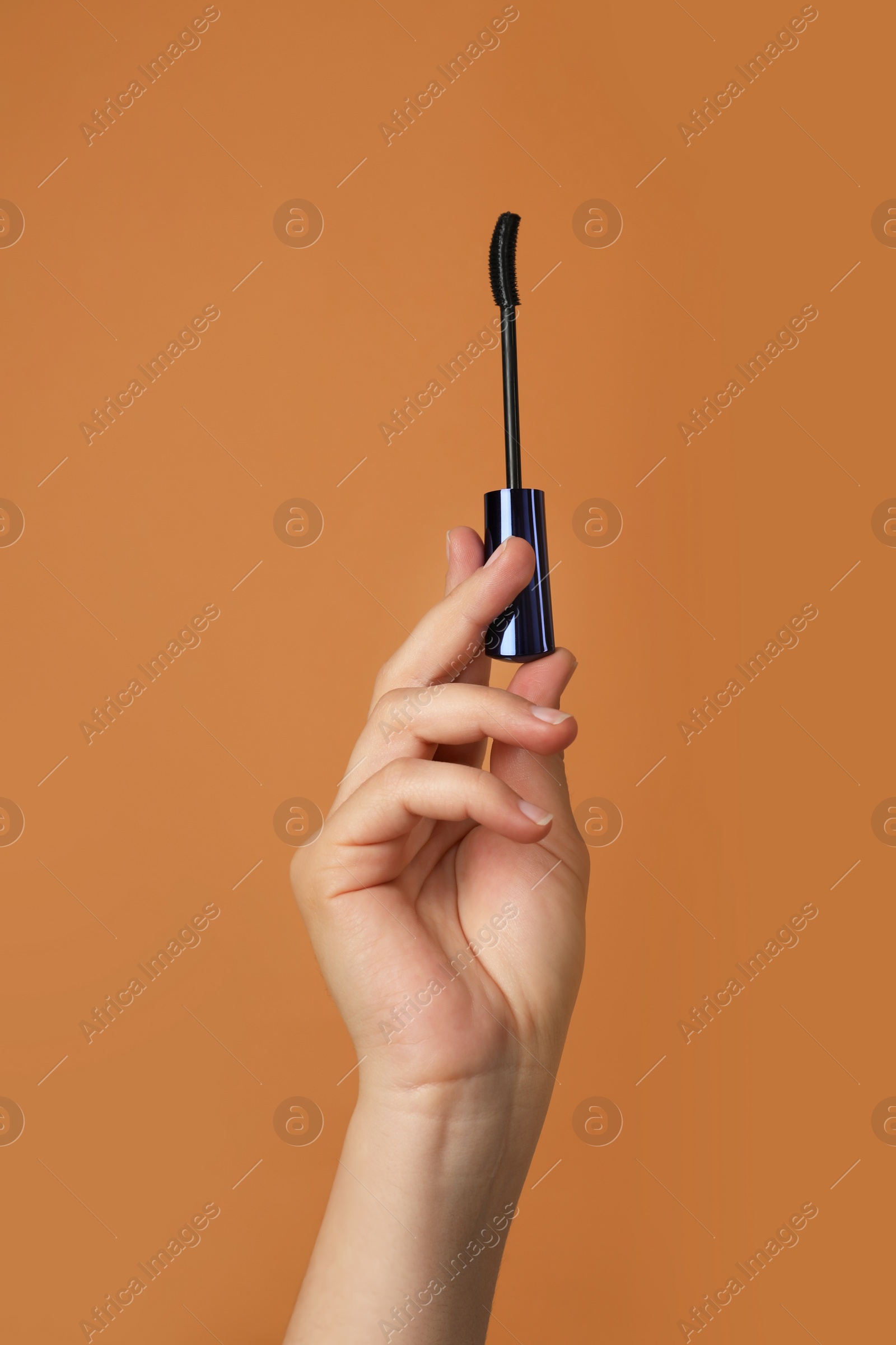 Photo of Woman holding mascara for eyelashes on light brown background, closeup