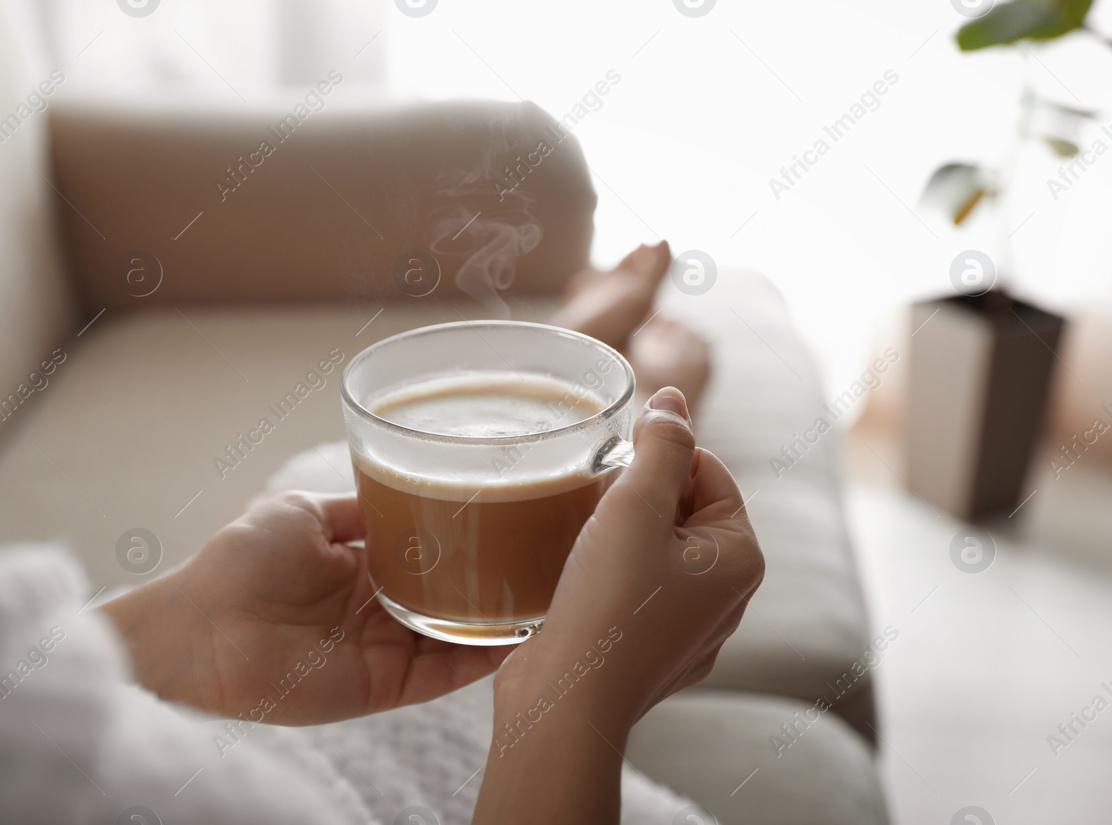 Photo of Woman with cup of hot drink on sofa at home in morning, closeup