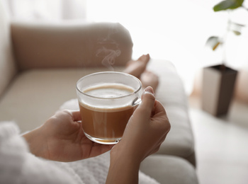 Photo of Woman with cup of hot drink on sofa at home in morning, closeup