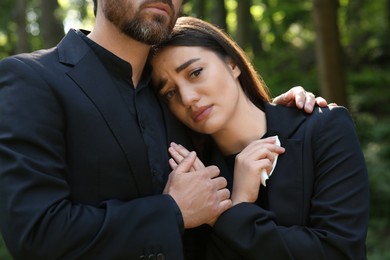 Photo of Sad couple in black clothes mourning outdoors. Funeral ceremony