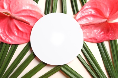 Creative composition with tropical flowers, green foliage and card on light background, top view