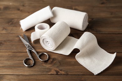 Photo of Medical bandage rolls, sticking plaster and scissors on wooden table