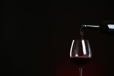 Photo of Pouring wine from bottle into glass on dark background, space for text