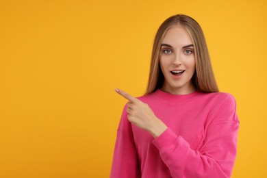 Photo of Special promotion. Emotional woman pointing at something on orange background, space for text