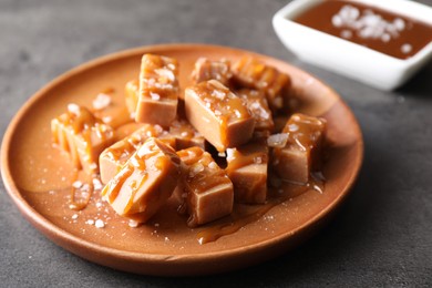 Photo of Plate with tasty candies, caramel sauce and salt on grey table, closeup