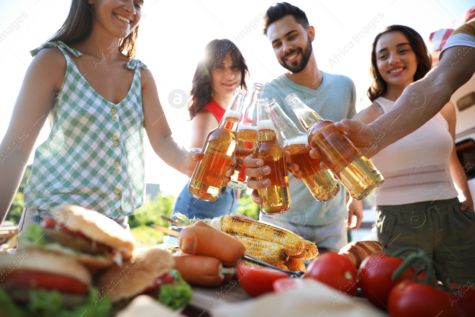 Photo of Happy friends toasting with bottles of beer outdoors. Camping season