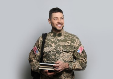 Photo of Cadet with backpack and books on light grey background. Military education