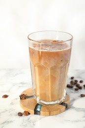 Photo of Refreshing iced coffee with milk in glass and beans on white marble table