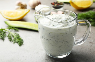 Photo of Glass jug of Tzatziki cucumber sauce with ingredients on table. Space for text