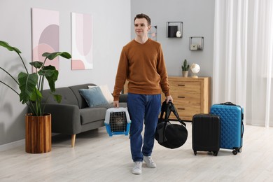 Photo of Travel with pet. Man holding carrier with cute cat and bag at home