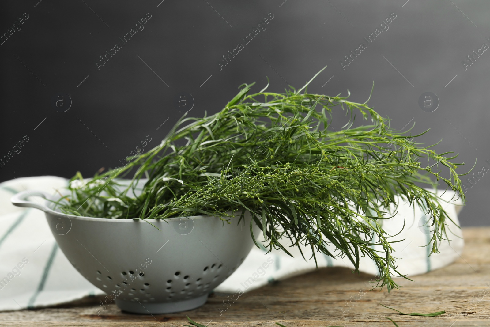 Photo of Fresh tarragon sprigs in colander on wooden table