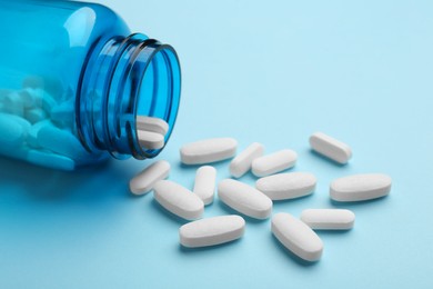 Photo of Vitamin pills and bottle on light blue background, closeup