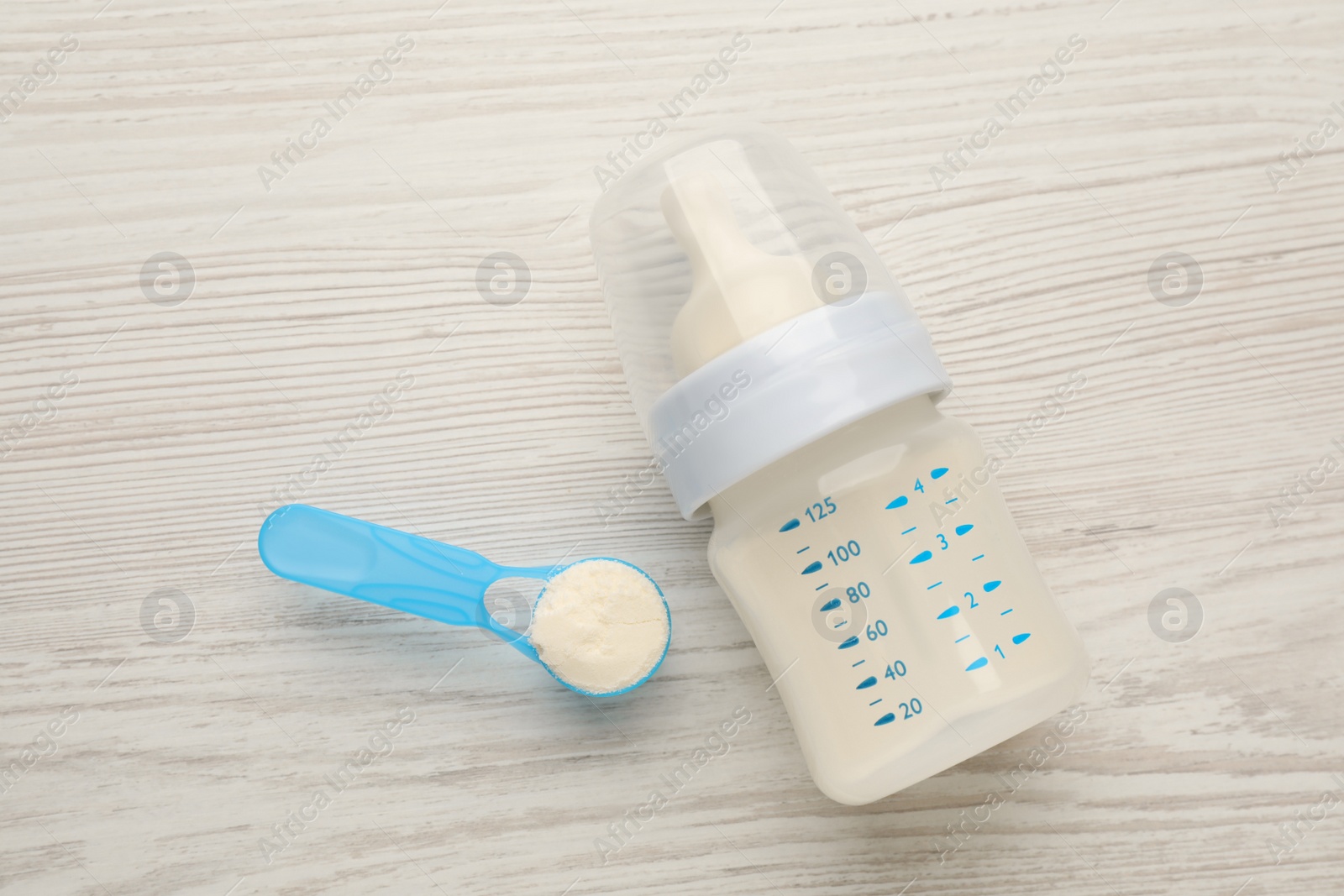 Photo of Feeding bottle with infant formula and powder on white wooden table, flat lay