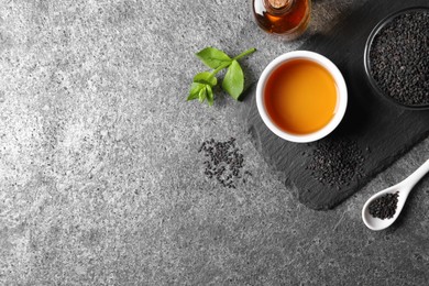 Photo of Black sesame seeds and oil on grey table, flat lay. Space for text