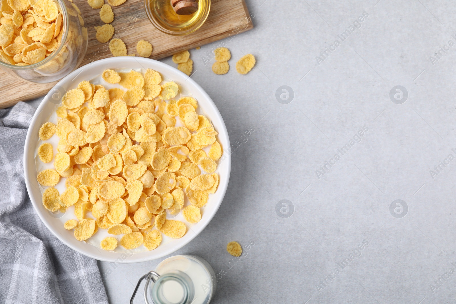 Photo of Breakfast cereal. Corn flakes and milk in bowl on light grey table, flat lay. Space for text