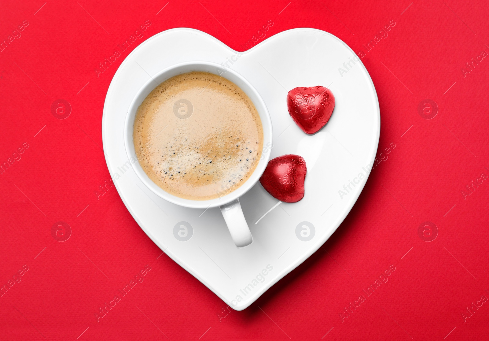 Photo of Cup of coffee and chocolate candies on red background, top view. Valentine's day breakfast