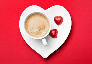 Cup of coffee and chocolate candies on red background, top view. Valentine's day breakfast