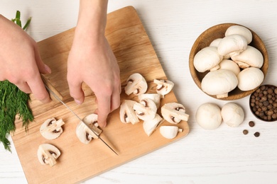 Photo of Young woman cutting fresh champignon mushrooms on wooden board, top view