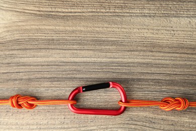 One metal carabiner with ropes on wooden table, top view. Space for text